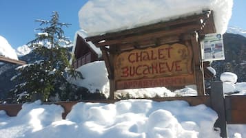 Ein hölzernes Schild mit dem Schriftzug "CHALET BUCANEVE APPARTAMENTI" in einer verschneiten Berglandschaft.