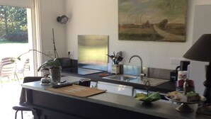 A modern kitchen with a central island, a dining area with a chair, and a large window.