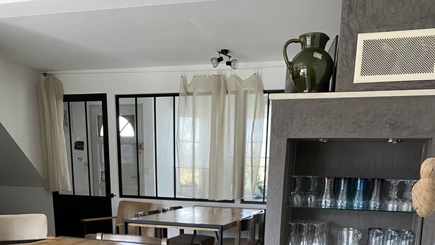 A dining area with a wooden table and chairs, a kitchen area with a sink and cabinets, and a shelf with glassware.