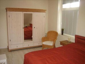 Quarto com um guarda-roupa grande, uma cama de solteiro, uma cadeira e janela com persianas.