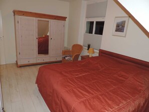 A bedroom with a bed, a wardrobe, a chair, a table with a lamp, and a window with blinds.