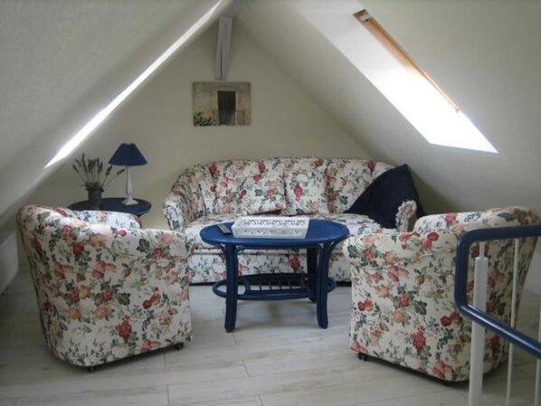 Une petite pièce chaleureuse avec un plafond en pente, un canapé à motifs floraux, une petite table et une lampe.