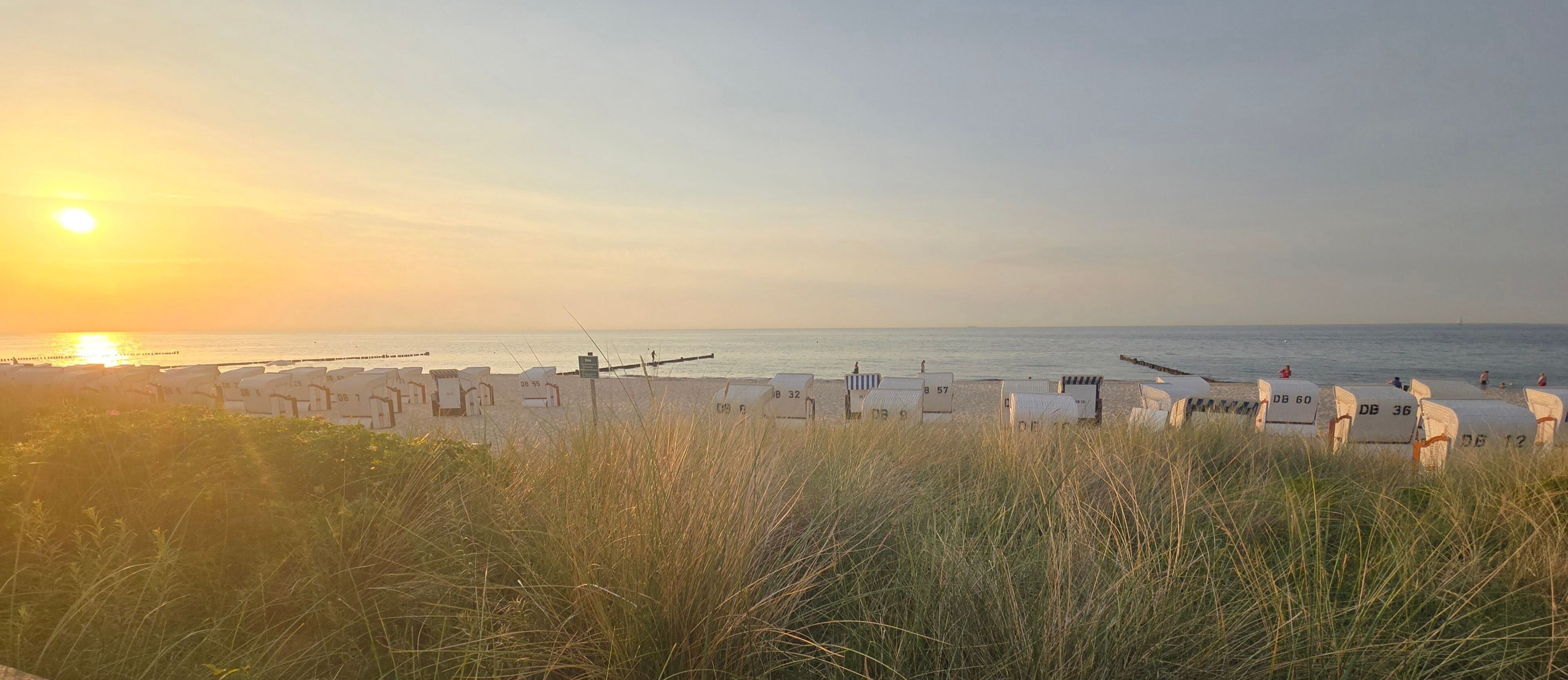 A beach with rows of numbered beach huts and a sunset in the background.