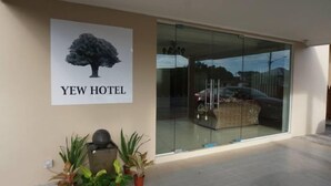Entrada d'hotel amb una porta de vidre, un cartell d'un arbre i plantes en testos.