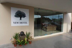 A hotel entrance with a glass door, a poster of a tree, and potted plants. - Yew Hotel (Miri)