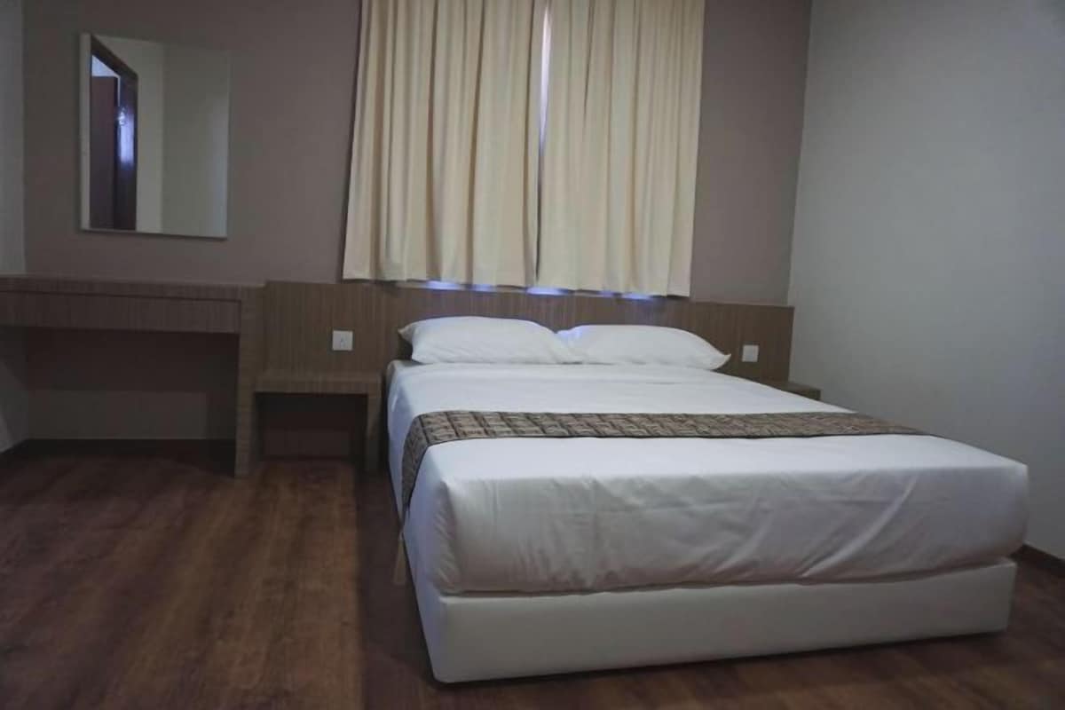 A hotel room with a bed, a bedside table, a mirror, and a window with curtains.