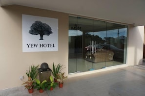 A hotel entrance with a glass door, a poster of a tree, and potted plants. - Yew Hotel (Miri)