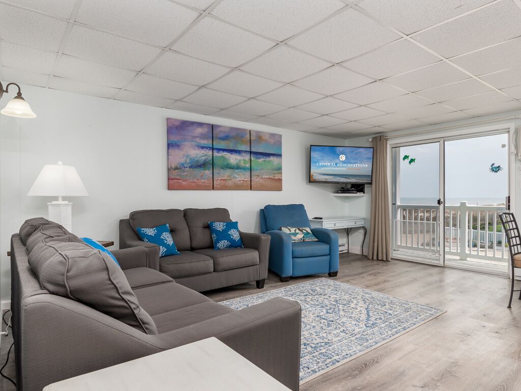 A living room with a grey sofa, a blue armchair, and a TV on the wall.