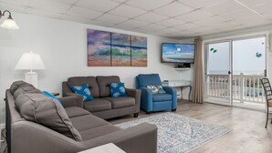 Een woonkamer met een grijze bank, een blauwe fauteuil en een televisie aan de muur.
