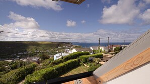 A view from a window overlooking a coastal town with houses, greenery, and a clear sky. - Spectacular one bedroom apartment , incredible coastal views, walk to the  beach (Porthtowan)
