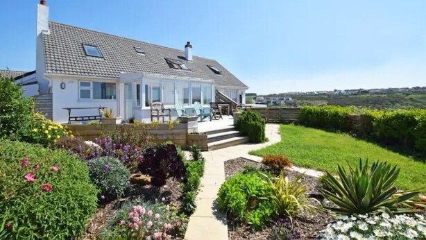 A house with a covered patio, a garden with various plants and flowers, and a clear view of the surrounding landscape. - Spectacular one bedroom apartment , incredible coastal views, walk to the  beach (Porthtowan)