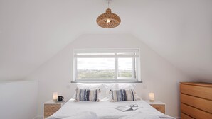 A bedroom with a large window, a bed with white linens, two bedside tables with candles, and a wooden dresser. - Spectacular one bedroom apartment , incredible coastal views, walk to the  beach (Porthtowan)