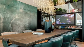 Un comedor moderno con una larga mesa de madera, sillas tapizadas en verde y un gran jarrón como centro de mesa.