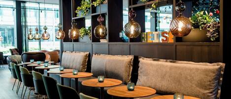 A modern interior with round tables, cushioned seating, and hanging decorative lights.