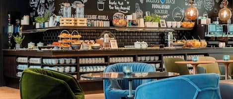 Ein Café mit einer Tafelwand, die verschiedene Sprüche und Zeichnungen zeigt, einer Theke mit Gebäck und Kaffeemaschinen sowie modern gestalteten Sitzplätzen.