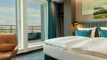 Ett hotellrum med en stor säng, en stol, utsikt över staden och en balkong.
