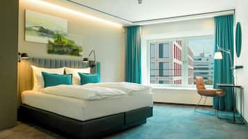 Ein modernes Hotelzimmer mit einem großen Bett, einem Schreibtisch und Blick auf Gebäude.