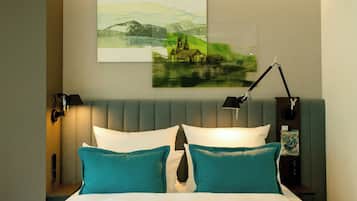 A neatly made bed with teal and white pillows, a headboard with a built-in lamp, and a wall-mounted artwork depicting a landscape.