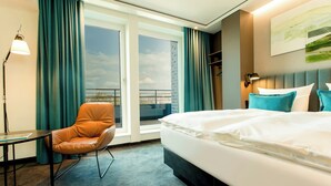 A hotel room with a bed, a chair, a table, and a view through a glass door.