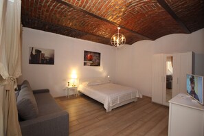 Ein Schlafzimmer mit Ziegeldecke, einem Bett, einem Nachttisch, einer Lampe, einem Fernseher und einem Kleiderschrank.
