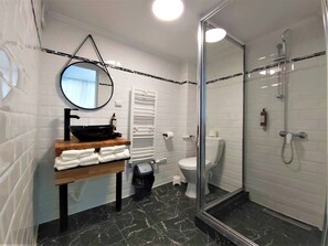 Ein Badezimmer mit einem schwarzen Waschbecken, weißen Fliesen, einem Spiegel, einer Toilette und einer Duschkabine.