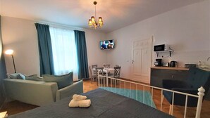 Habitación de hotel con cama, escritorio, silla, televisión y kitchenette.