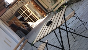 Un patio con mesas y sillas de madera, una cerca metálica y un edificio con ventana de celosía.