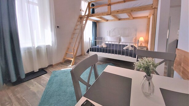 Una habitación con una cama litera, un escritorio con una computadora, una silla y una pequeña mesa con un florero.