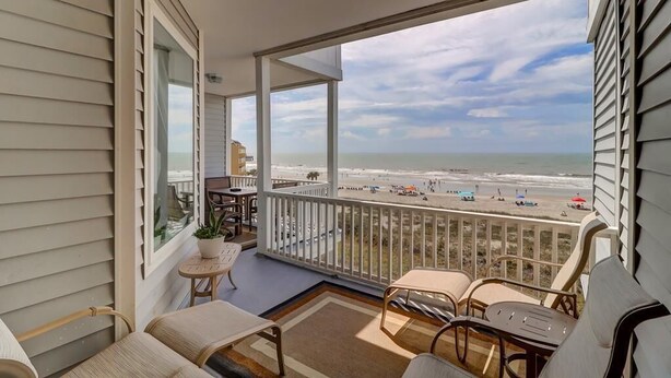 Un balcon avec vue sur la plage, des meubles d’extérieur et une plante en pot.