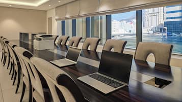 A modern conference room with a long table, multiple chairs, laptops, and a view of a cityscape through large windows.