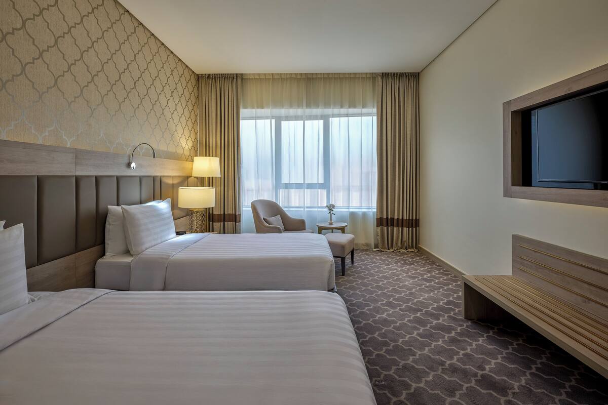 A hotel room with two beds, a TV, a desk, and a chair.