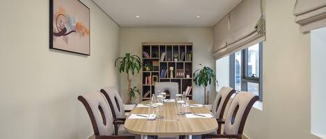 A dining area with a round table, four chairs, a bookshelf, and two potted plants.