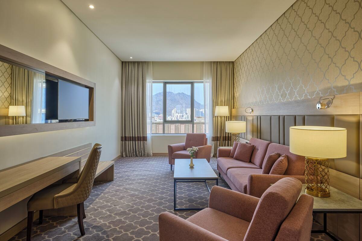 A hotel room with a large flat-screen TV, a sofa set, a desk, and a coffee table.