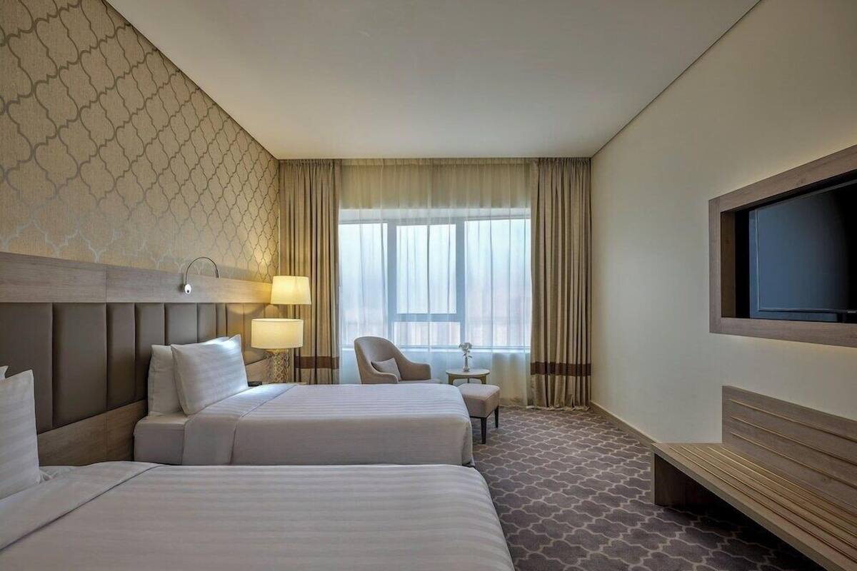 A hotel room with two beds, a TV, a desk, and a chair.