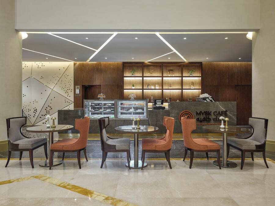 A modern cafe interior with a marble counter, wooden shelving, and contemporary chairs.