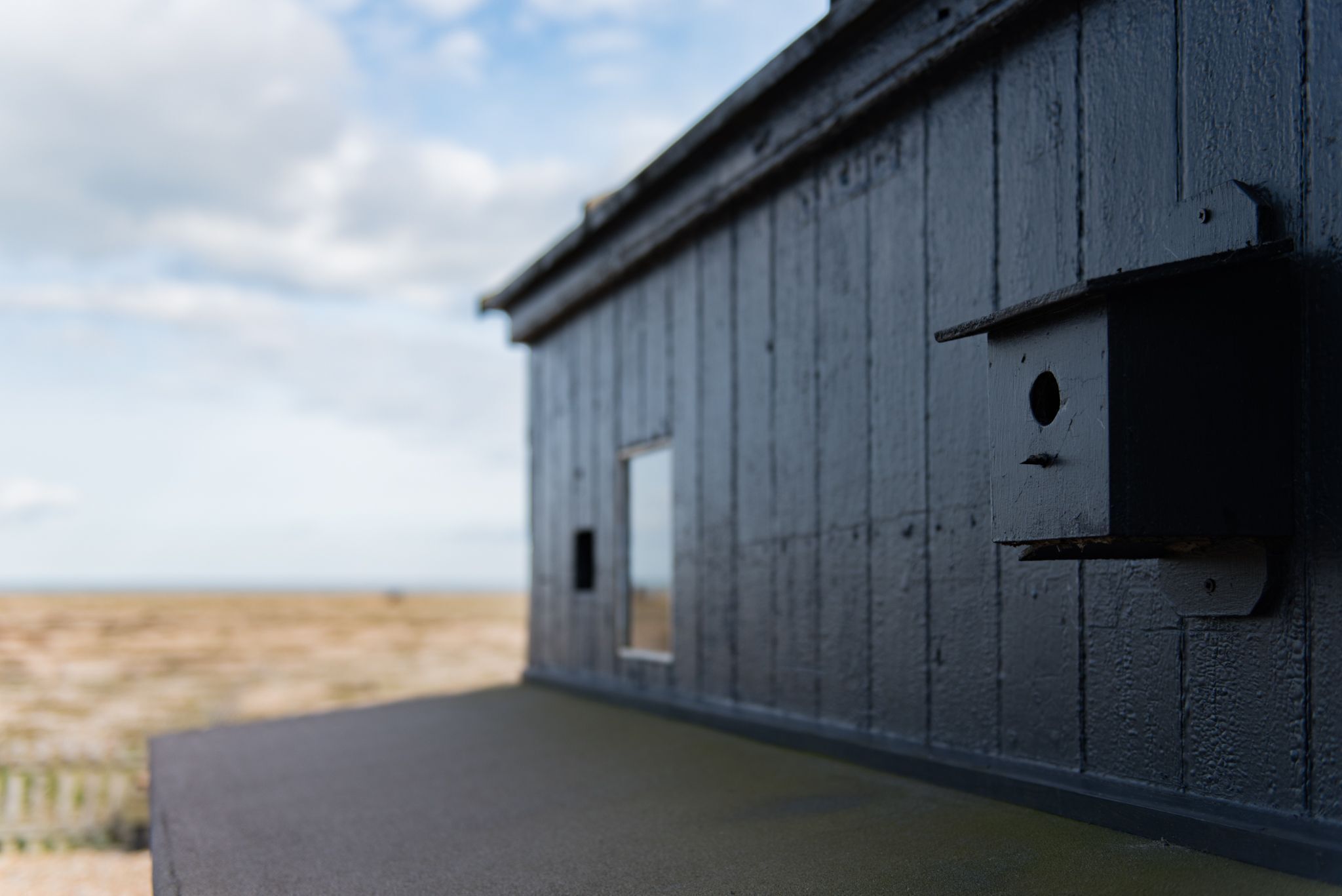 Une vue rapprochée d’une structure en bois, dotée d’une fenêtre et d’une porte, sur fond de plage.