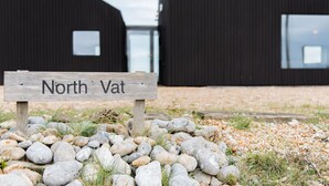 Un letrero de madera con la inscripción 'North Vat', sobre una superficie de grava con rocas y hierba.