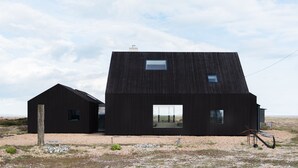 Un edificio moderno negro con techo inclinado y ventanas grandes, ubicado sobre superficie de grava con un letrero que dice "North Vat".