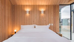 Un dormitorio moderno con paneles de madera, una cama grande, dos luces fijadas a la pared y vistas a través de un ventanal.
