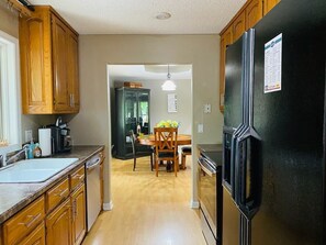 A kitchen with wooden cabinets, a black refrigerator, a dining table with chairs, and a light fixture above the table.