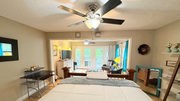 A bedroom with a bed, a desk, a chair, a ceiling fan, and a window with curtains.