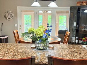 A dining area with a granite table, chairs, a glass vase with flowers, and a cabinet with glass doors. - Lakefront living at its best - a guest favorite! (Hot Springs Village)