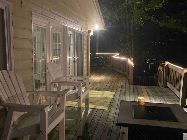 A wooden deck with chairs and a table, a covered area with glass doors, and a railing.