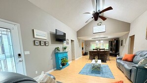 A spacious living room with a fireplace, a ceiling fan, and a television mounted on the wall.