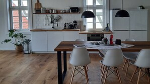 Eine moderne Küche mit Holzbalken, weißen Schränken und einem Essbereich mit Holztisch und weißen Stühlen.