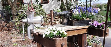 A rustic outdoor setting with a wooden table, vintage Singer sewing machine, and various potted plants.