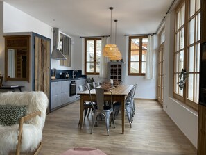 A modern kitchen with a dining area, large windows, and a wooden dining table.