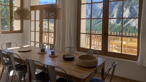 Ein Essbereich mit Holztisch, Metallstühlen und Blick auf Berge durch große Fenster.