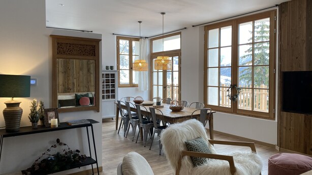 Ein geräumiges Wohnzimmer mit einem Holzespeise-Tisch, bequemen Sitzgelegenheiten, großen Fenstern mit Blick und einem an der Wand befestigten Flachbildfernseher.