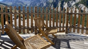Eine Holterrasse mit Korbstühlen mit Blick auf eine gebirgige Landschaft.